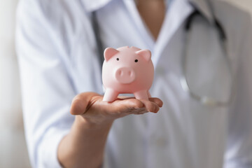 Close up young woman wearing white coat with stethoscope, doctor therapist physician gp holding pink piggy bank, hospital budget, healthcare money savings and medical insurance concept