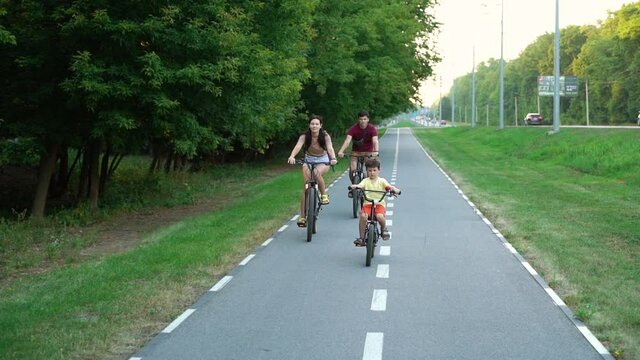 Biker family riding on bike lane near city road, roller skater with poles passing by. Tracking shot of active parents and little son enjoying sports on summer day. Concept of lifestyle