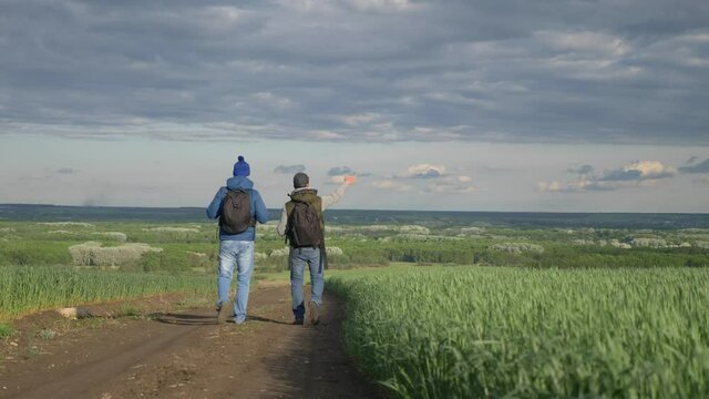 teamwork travel. two man hikers with backpacks walk along a trail next to a field with green grass in nature. concept adventure travel hiking healthy. two lifestyle tourists walk walking talking