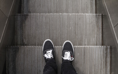 Man standing on escalator in a sneaker shoes.