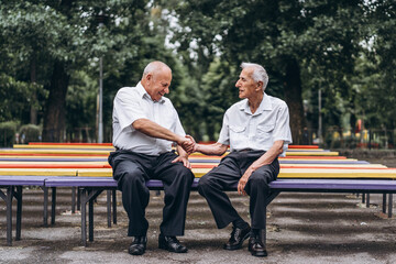 Two old senior adult men have a conversation outdoors in the city park.