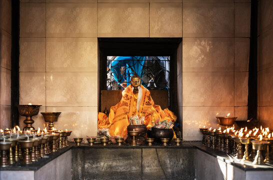 A gilded statue of Buddha, covered with a orange hadak, stands on an altar surrounded by lighted oil lamps to offer fire.