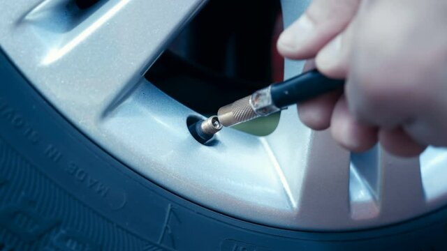 The driver unscrews the nipple cap of the wheel of his car, screw on the hose from the pump and inflates the wheel. Closeup
