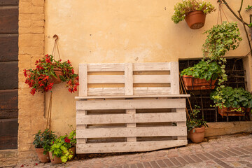 bench made of pallets with flowers in baskets on the wall. Toscane Italy