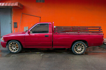 An old red truck parked beside an orange wall.