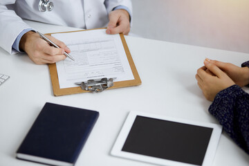 Fototapeta premium Friendly red-bearded doctor and patient woman discussing current health examination while sitting in sunny clinic. Medicine concept