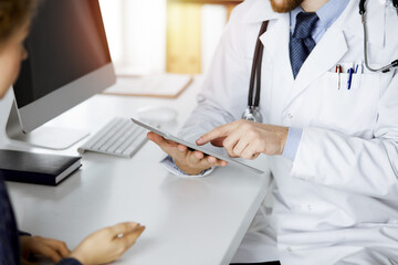 Unknown red-bearded doctor and patient-woman discussing current health examination while sitting...