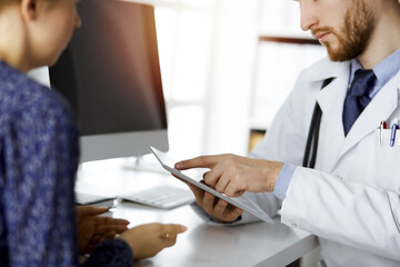Unknown red-bearded doctor and patient-woman discussing current health examination while sitting...