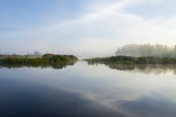 Beautiful morning sunrise over blue forest lake with reeds and reflection of clouds
