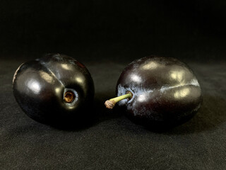 Two blue plums on a black background. A couple of ripe plums in a plate. Fruit tree fruit.