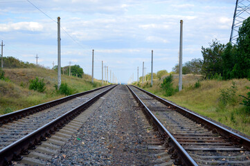 Fototapeta na wymiar two railway tracks go into the distance, trees grow along the edges, and above there is a blue sky with white clouds
