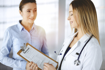 Young woman-doctor and her patient are discussing patient's current health examination, while...