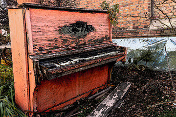 Old broken red piano with peeled paint from rain and wind, outside on an autumn day. Discarded...