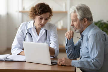 Confident doctor consulting mature patient at appointment, explaining, showing medical checkup...