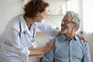 Smiling young nurse caregiver supporting mature patient during homecare visit, friendly woman...