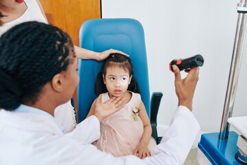 Doctor checking eyes of little girl with flashlight in medical room at the hospital