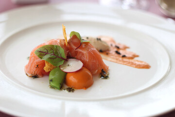 Close up of a plate of delicious smoke salmon served with fresh vegetable salad and delicious sauce, soft focus