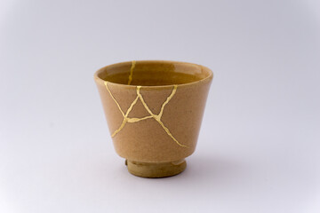Kintsugi beige sake cup. Gold cracks restoration on old Japanese pottery restored with the antique...