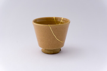 Kintsugi beige sake cup. Gold cracks restoration on old Japanese pottery restored with the antique Kintsugi restoration technique. The beauty of imperfections. 