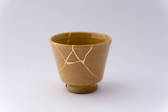 Kintsugi beige sake cup. Gold cracks restoration on old Japanese pottery restored with the antique Kintsugi restoration technique. The beauty of imperfections. 
