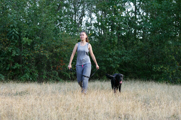 Young attractive sport girl walking with black Labrador in park. Healthy lifestyle. Walk with favorite pet in wood.