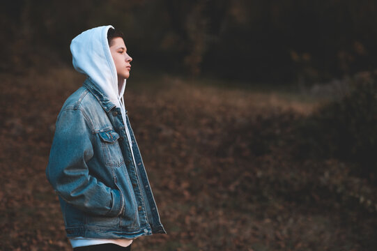 Handsome teen boy 15-16 year old wearing denim jacket and white hoodie standing outdoors over nature autumn background. Teenagerhood.