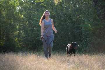 Young attractive sport girl walking with black Labrador in park. Healthy lifestyle. Walk with favorite pet in wood.