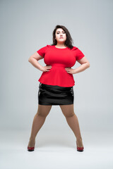 Plus size fashion model in red blouse and black skirt, fat woman on gray background, body positive concept