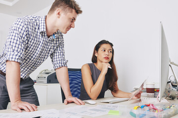 Serious young UI designers discussing sketches and layouts on computer screen when working on new project