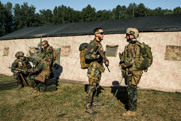 Officer with rifle preparing soldier for military operation and giving advice to him at military...