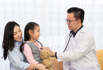 asian doctor in white coat using stethoscope to listen to heart and lung sound of young girl who is...
