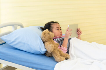 young asian girl is lying in the hospital bed and watching cartoon in tablet. healthcare and medical concept