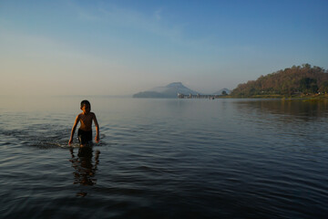 young asian boy walking in the lake in the morning