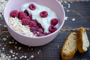 Healthy breakfast concept. Red raspberries with oats in pink bowl with toasts around. Dark wood background. soft focus