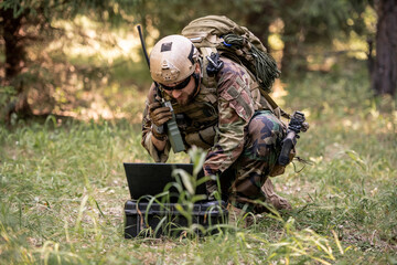 Bearded soldier in camouflage uniform sitting in forest and sending message through radio device...