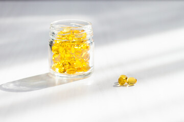 Yellow capsules with vitamin D, fish oil omega 3 with sunlight on white wooden background. Healthy...