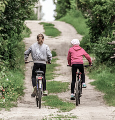 Obraz premium Two girls ride bicycles on a dirt road