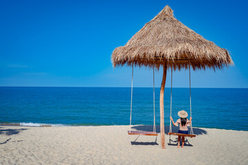 A woman on a swing under a wooden hut by the beach at Sichon beach, Nakhon Si Thammarat