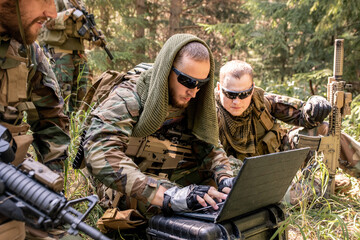 Concentrated army programmer in sunglasses using military computer while getting in touch with...