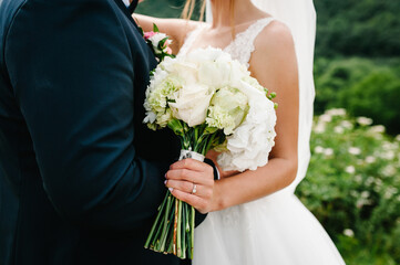 The bride and groom with a wedding bouquet, holding on hands and standing on wedding ceremony of the outdoor in the nature backyard.