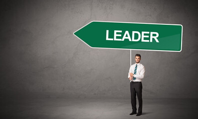 Obraz premium Young business person in casual holding road sign with LEADER inscription, new business direction concept