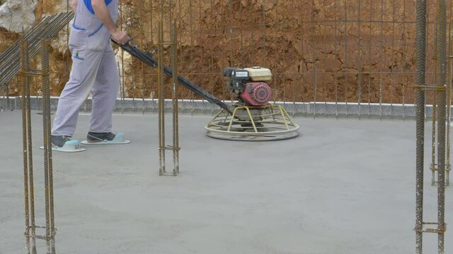 SLOW MOTION, CLOSE UP: Unrecognizable contractor polishes drying concrete slab with a heavy industrial machine. Builder wearing protective slippers buffs the rough surface of drying concrete slab.