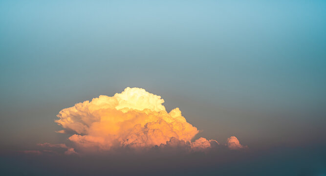 A photograph of a large golden-yellow cloud in the twilight colored sky in the evening. Its edges are wavy and fluffy with a soft blue backdrop. Feeling calm and relax. There is a copy space on top.