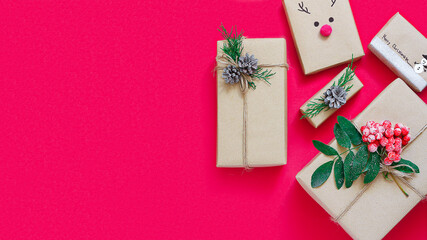 Christmas composition of gift boxes in craft paper on a red background.The concept of zero waste.Eco-friendly natural decor for packaging Christmas gifts.flat lay.copy space.banner