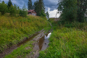Dirt road with mud and puddles in a village with abandoned old wooden houses in northern Russia