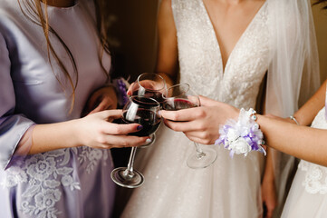 Gorgeous bride and bridesmaids toasting with wine and having fun on wedding morning. Hands holding...