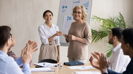 Smiling middle aged 60s female company leader shaking hands with happy young arabic colleague,...