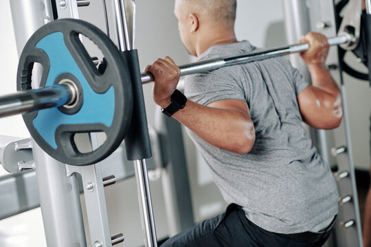 Mature muscular man doing squats with large barbell with heavy weight plates
