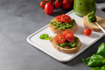 homemade bruschetta with fresh pesto and cherry tomatoes on a dark background with food ingredients. healthy plant-based food recipes concept. space for text