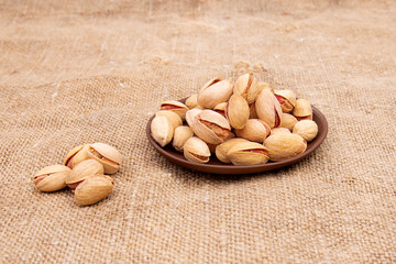 Nuts pistachios in a wooden spoon and a brown earthenware plate on old burlap